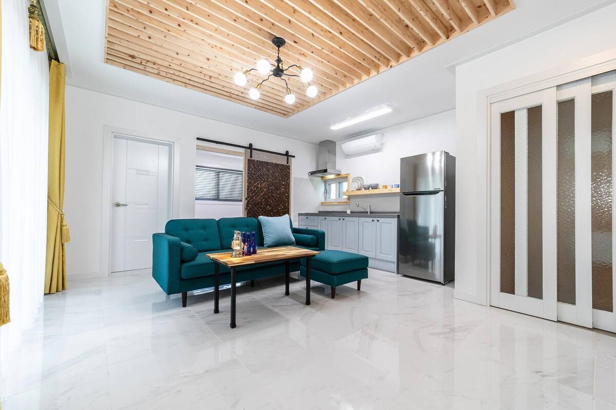 A modern kitchen with a stainless steel refrigerator, a wooden ceiling, and a teal sofa set.