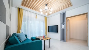 A modern living room with a teal sofa, a wooden ceiling, a TV mounted on a wall, and a small table with bottles. - Pohang Ohdoheal Poolvilla (Pohang)