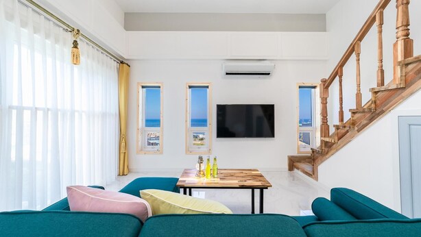A living room with teal sofas, a wooden staircase, and a TV mounted on the wall. - Pohang Ohdoheal Poolvilla (Pohang)