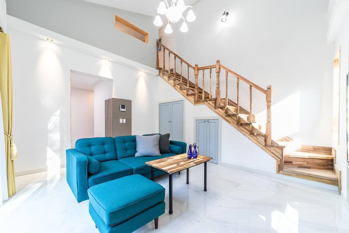 A spacious living area with a blue sectional sofa, a wooden coffee table, and a staircase with wooden railings.