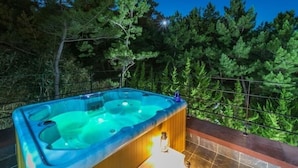 A hot tub with a wooden surround and a tiled floor, surrounded by a metal fence and trees. - Pohang Ohdoheal Poolvilla (Pohang)