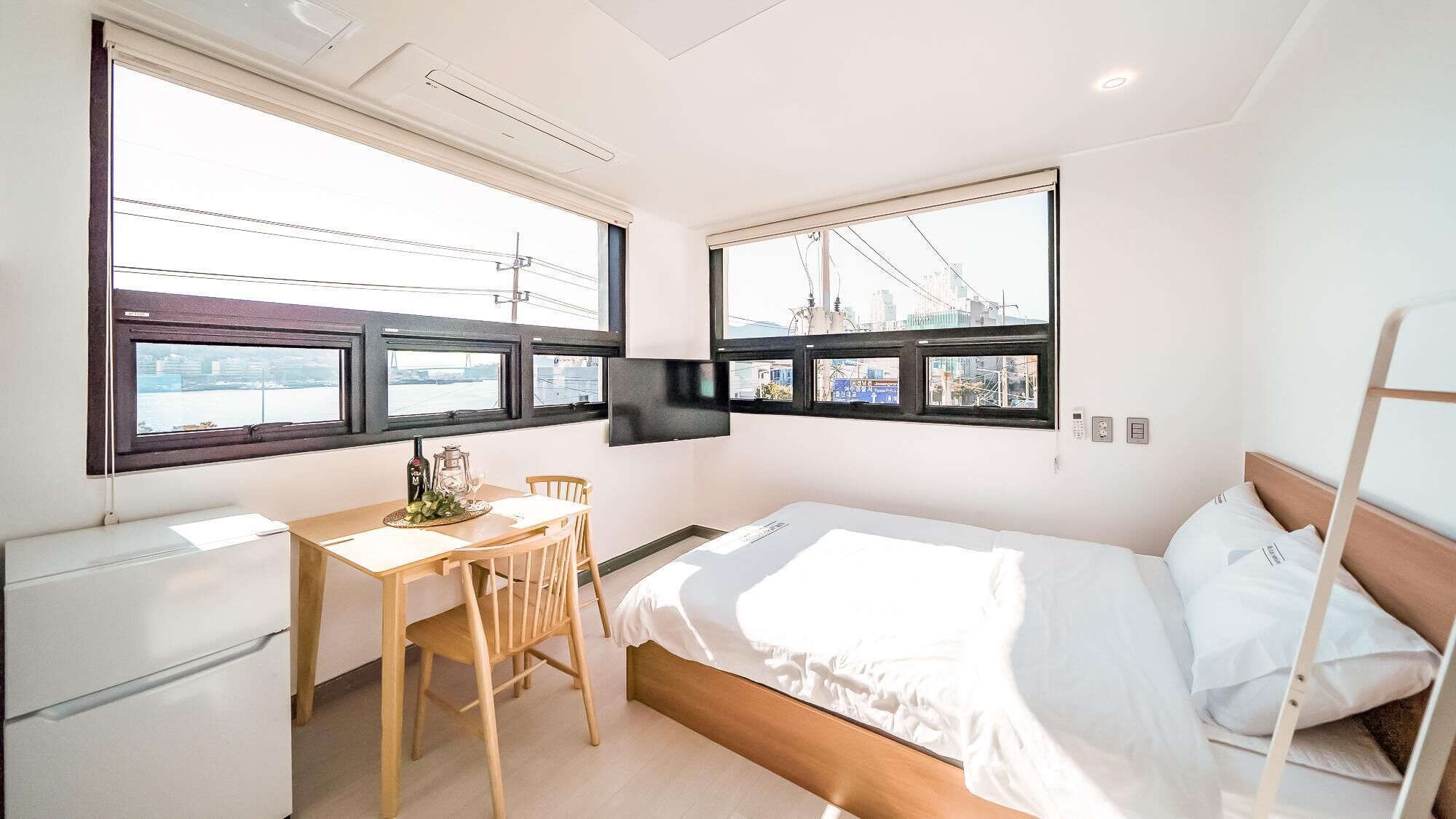 Ein kompaktes Hotelzimmer mit Bett, Schreibtisch und Stuhl. Zwei Fenster bieten Blick auf die Stadt.