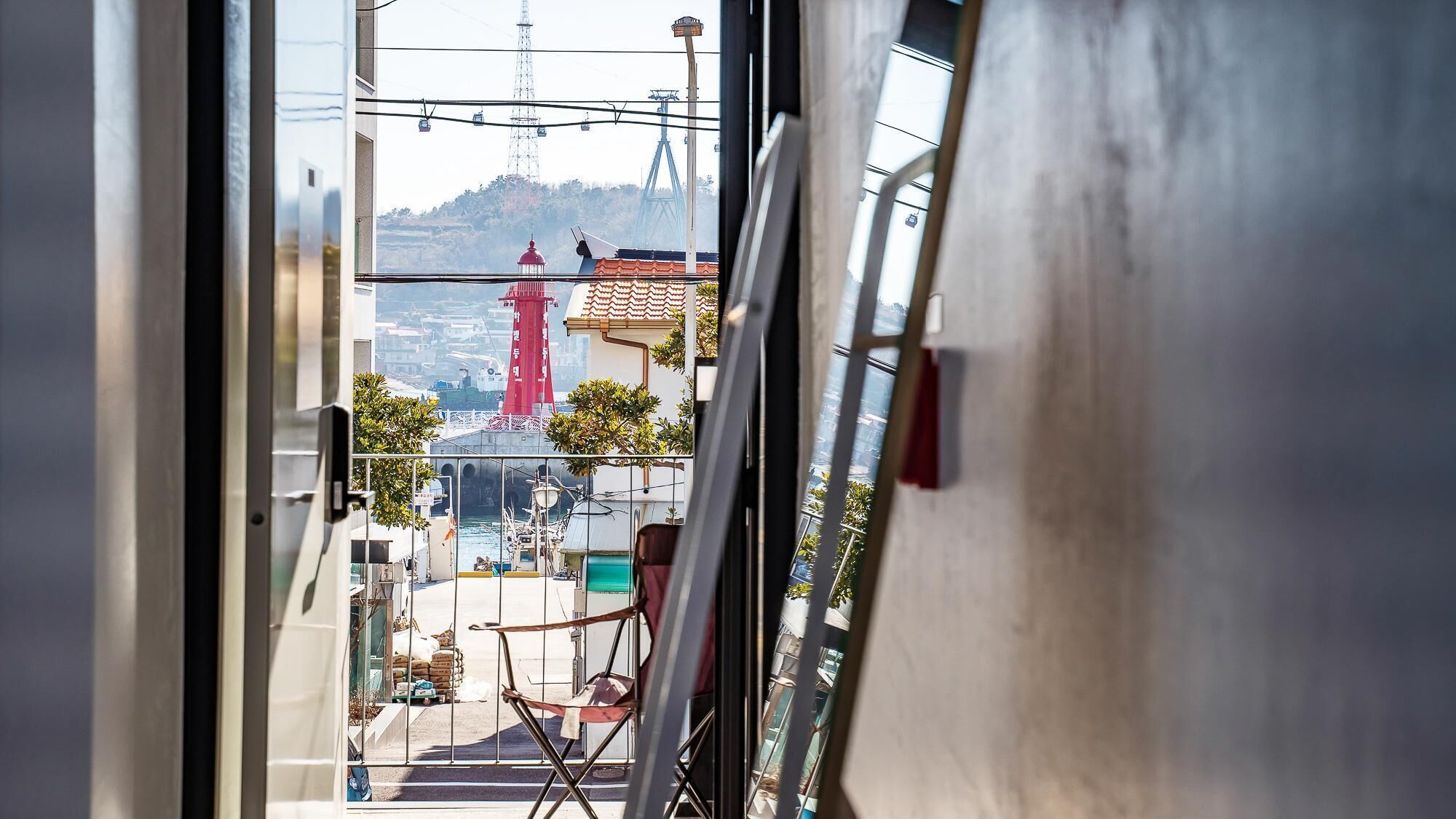 Blick durch ein Fenster auf einen Raum mit Stuhl, Tisch und Ansicht eines roten Turms sowie eines Schiffes.