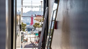 A view through a window of a room with a chair, a table, and a view of a red tower and a ship. - Yeosu Nangmanstay Pension (Yeosu)