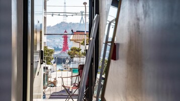 A view through a window of a room with a chair, a table, and a view of a red tower and a ship.