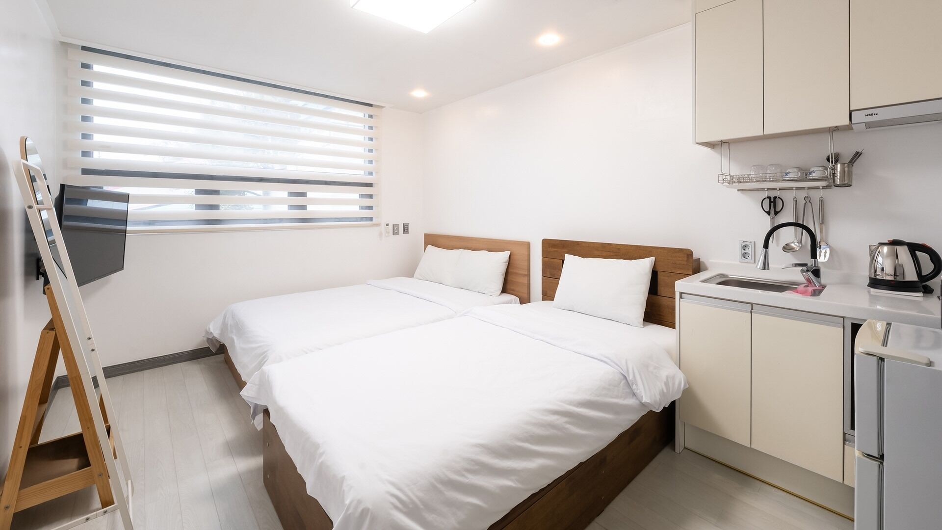 Une chambre d’hôtel équipée d’un lit, d’une télévision, d’une kitchenette et d’une fenêtre avec des stores.