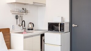 Een kleine keuken met een magnetron, waterkoker en een houder voor keukengerei.