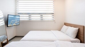 Een hotelkamer met twee bedden, een televisie aan de muur en een raam met jaloezieën.