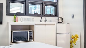 Una kitchenette compacta con microondas, un refrigerador pequeño, un lavamanos y una ventana arriba.