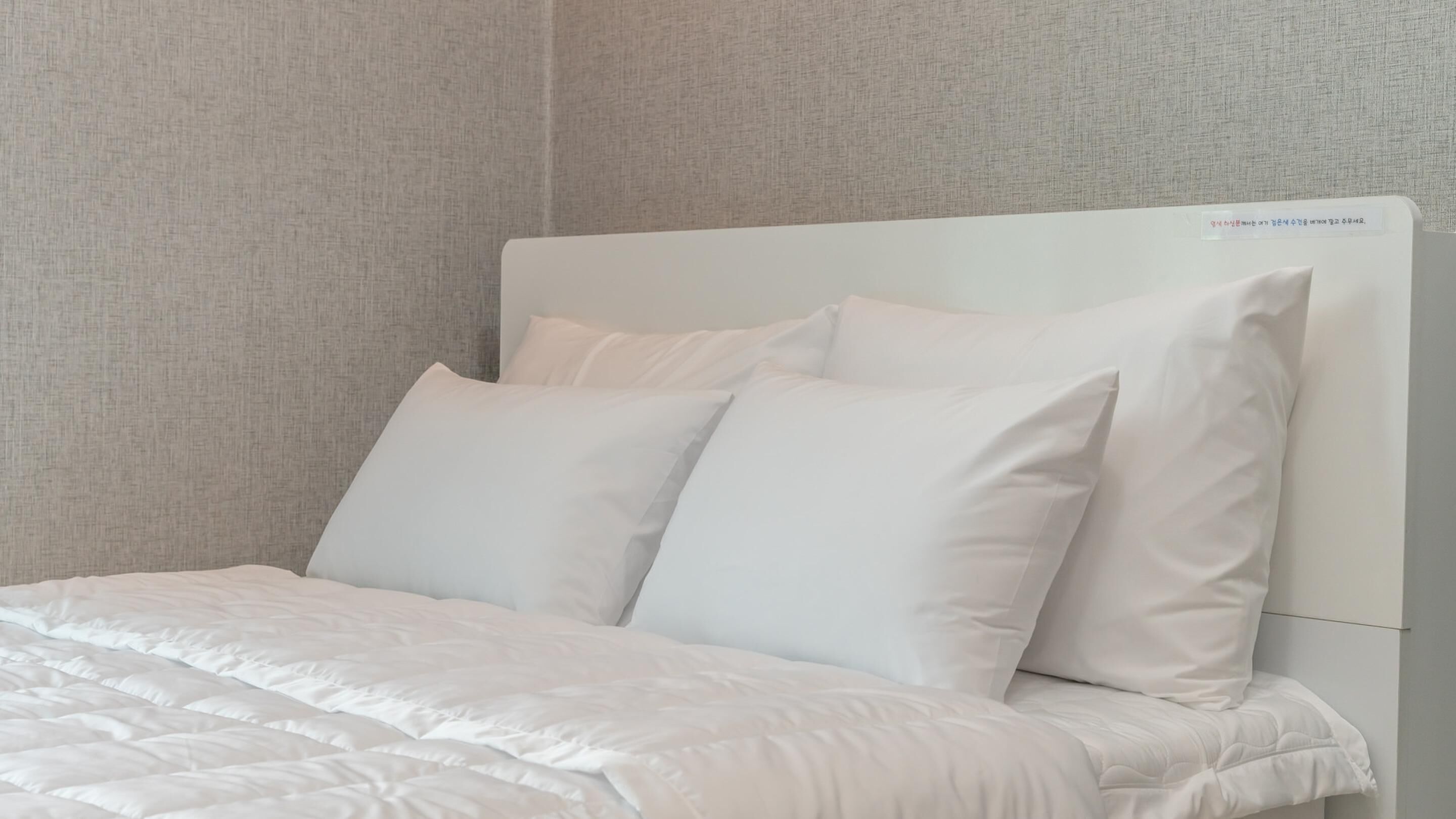 A bed with white bedding and pillows, a headboard, and a textured wall.