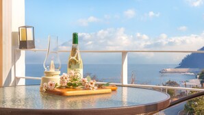 Ein Glastisch mit einer Weinflasche, einer Kerze und Blumen auf einem Balkon mit Blick aufs Meer.