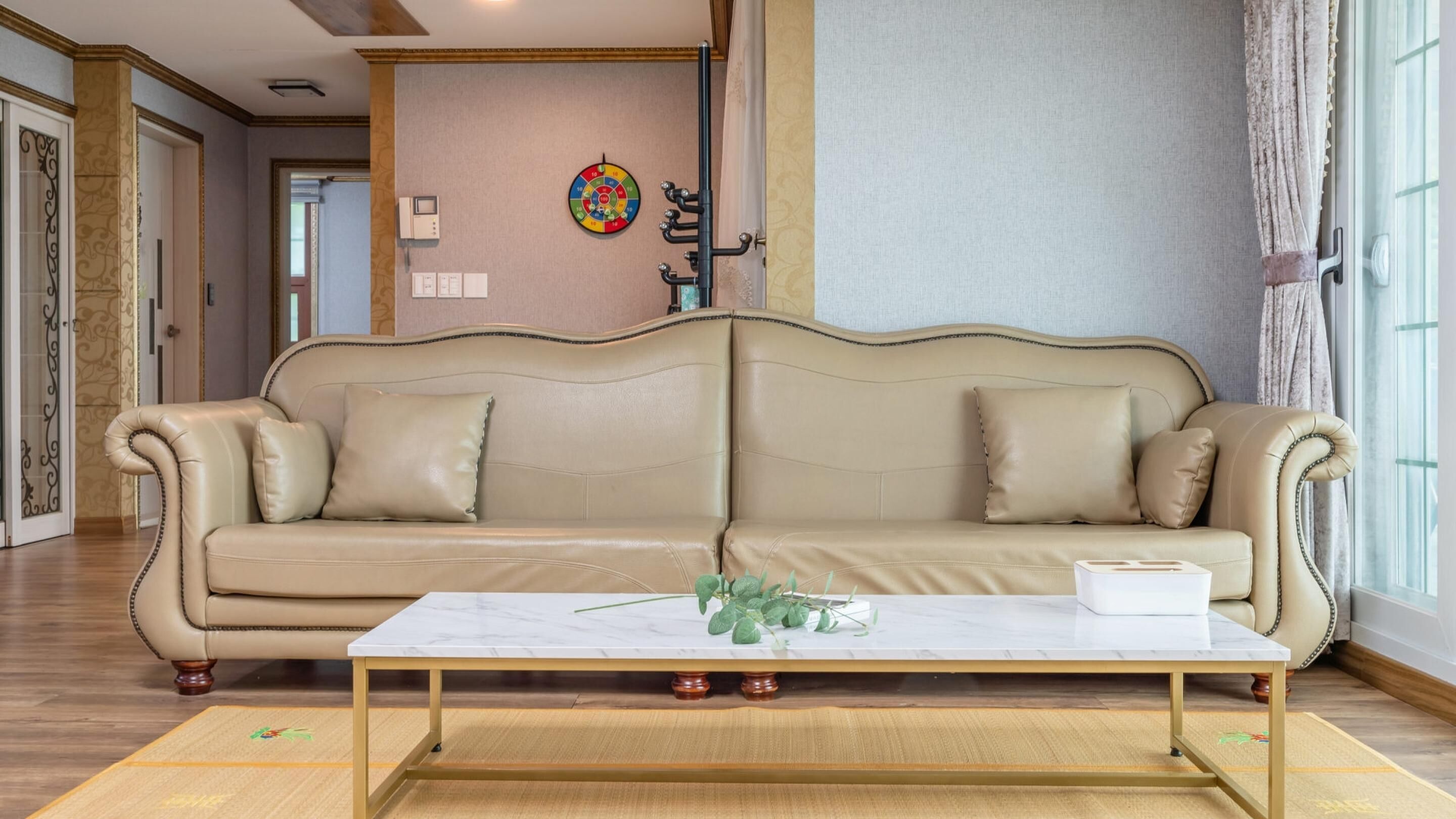 Un salon spacieux avec un canapé beige, une table basse en marbre et une horloge murale décorative.