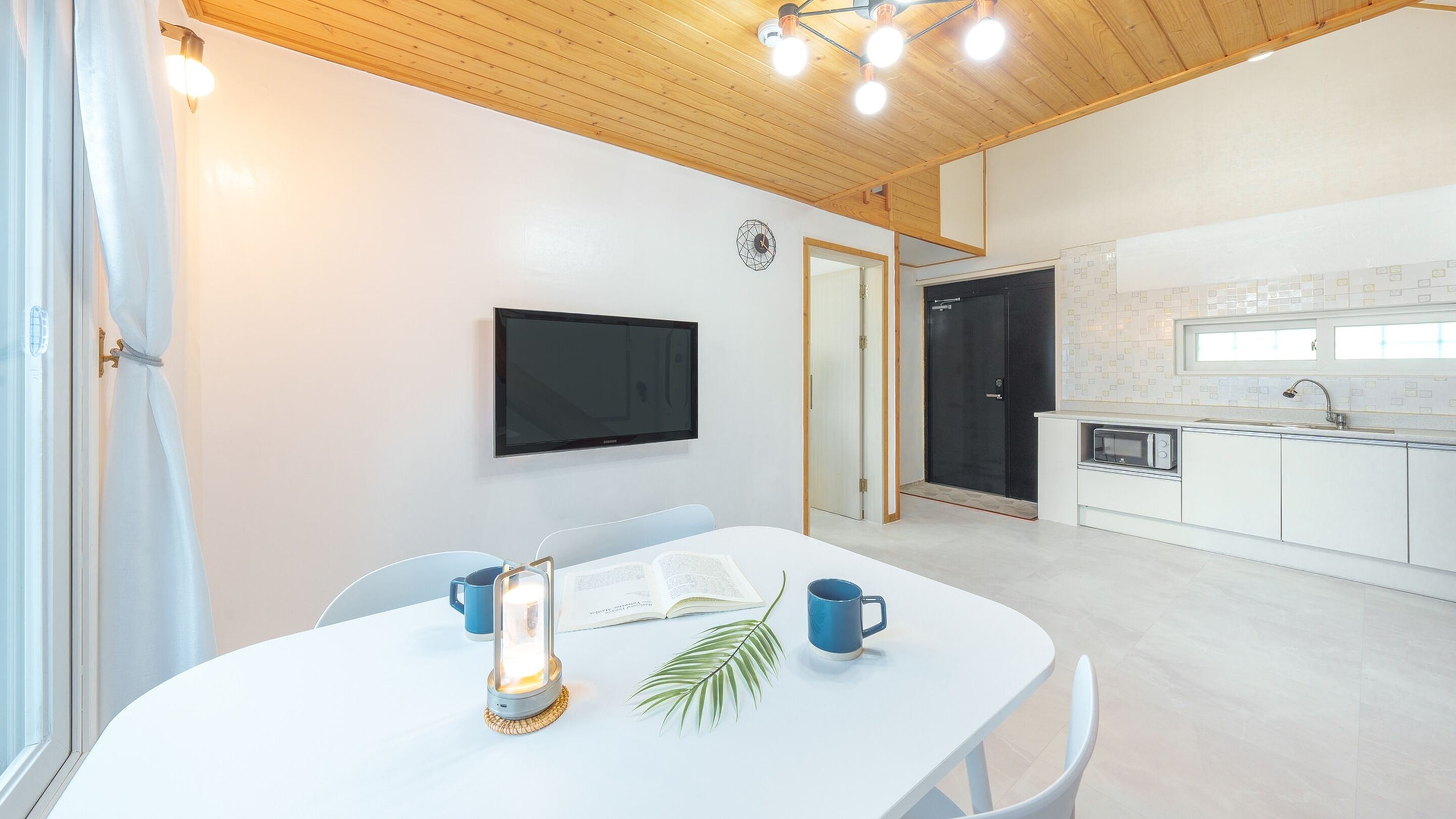 A modern kitchen with white cabinets, a black door, and a window above the sink.