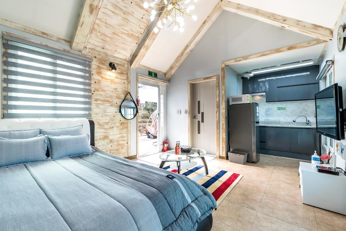 A modern bedroom with a large bed, a small table, and a kitchenette.