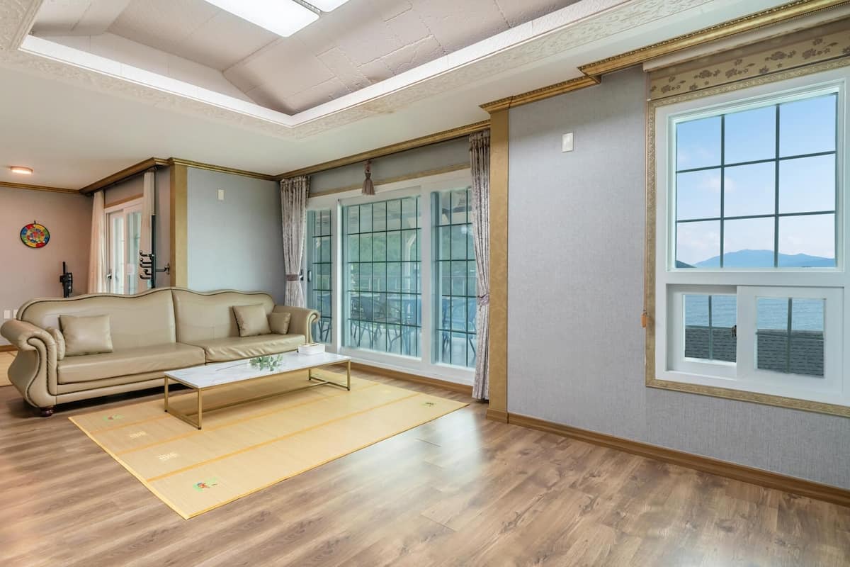 A spacious living room with a beige sofa, a coffee table, and a large window offering a view of the outdoors.