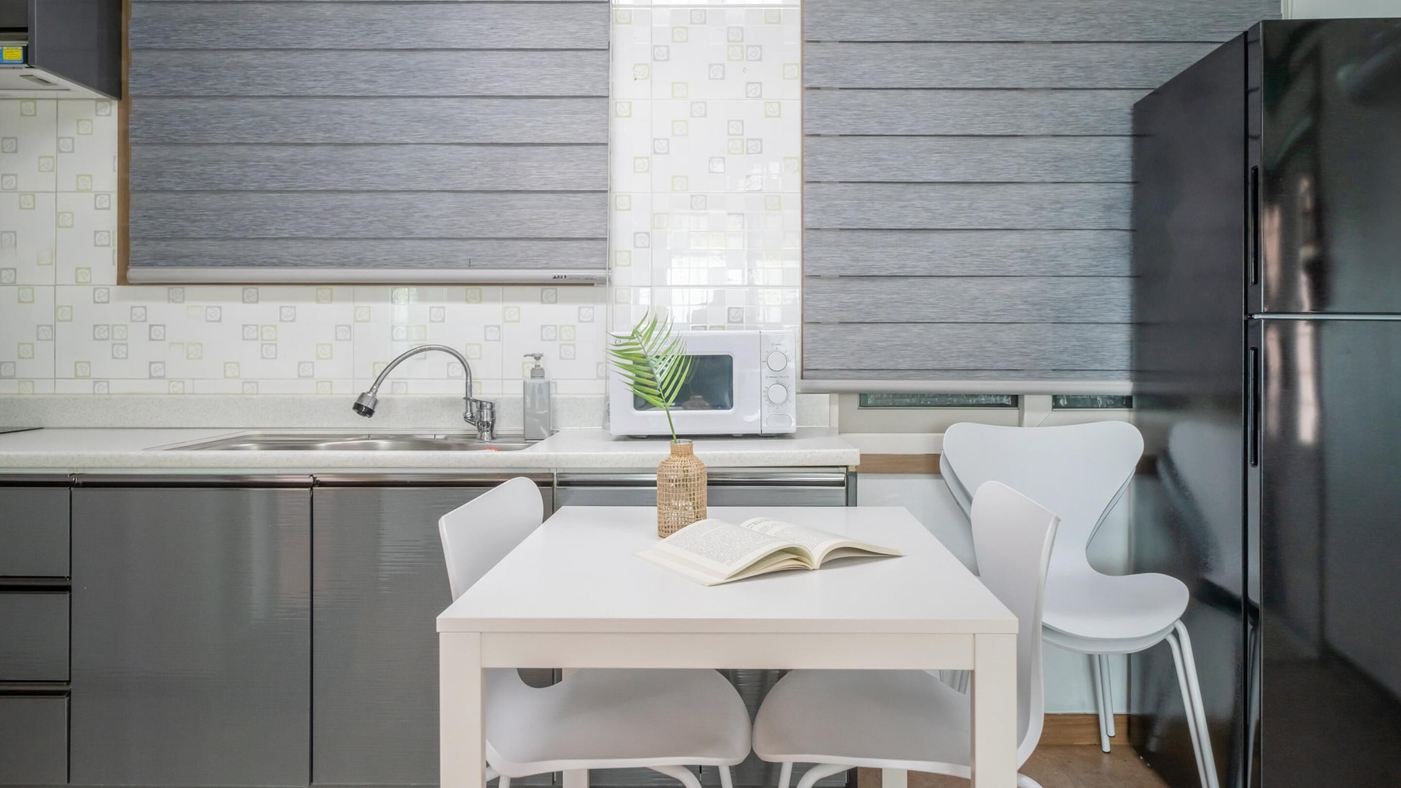 Une cuisine moderne avec une table blanche, deux chaises, un four à micro-ondes et un réfrigérateur en acier inoxydable.