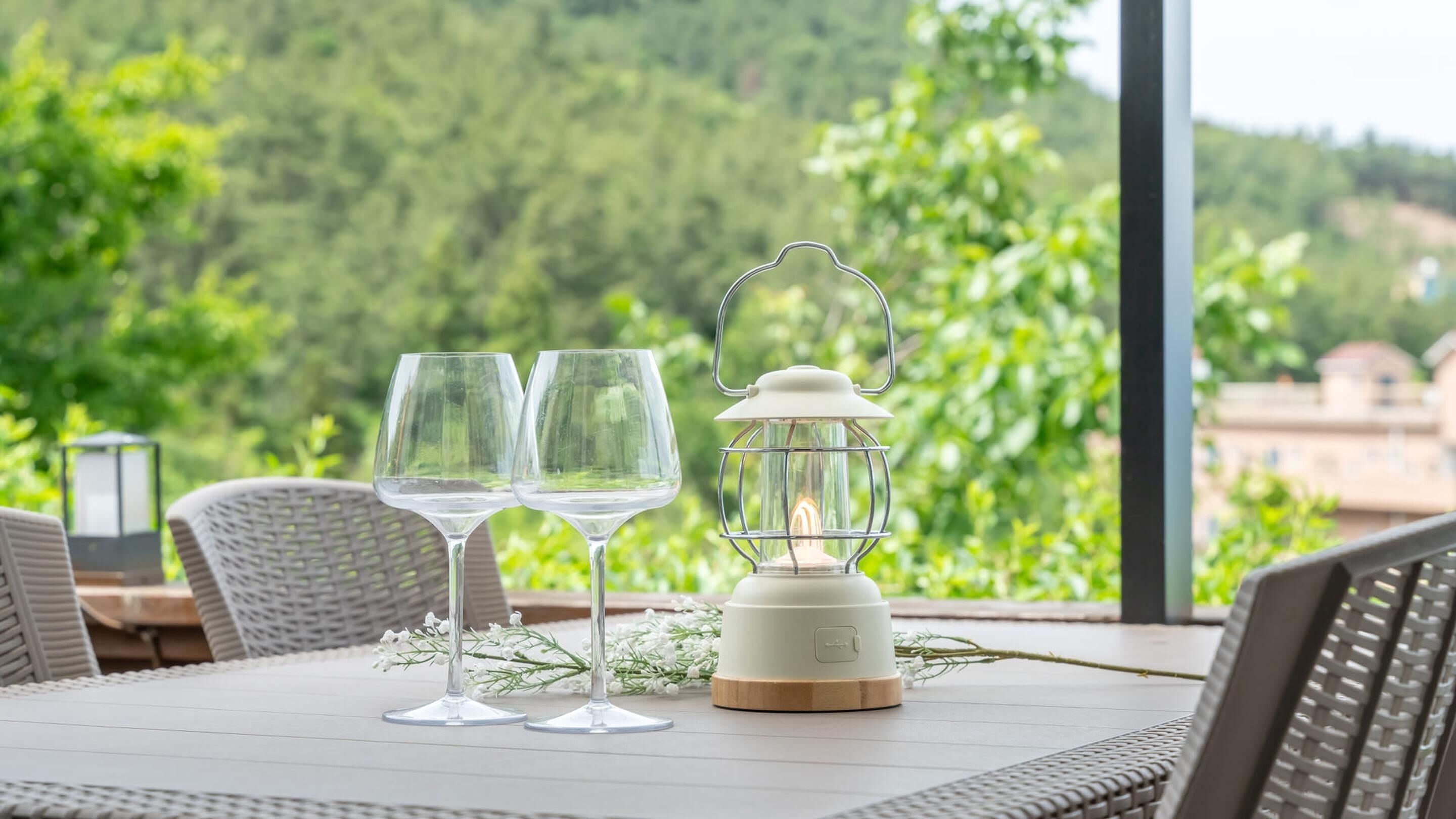 Una mesa con dos copas de vino y un farol, al aire libre con vistas a zonas verdes y edificios.