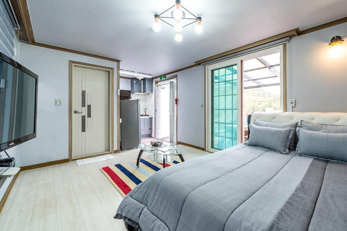 A bedroom with a bed, a television, a desk, a chair, and a window.