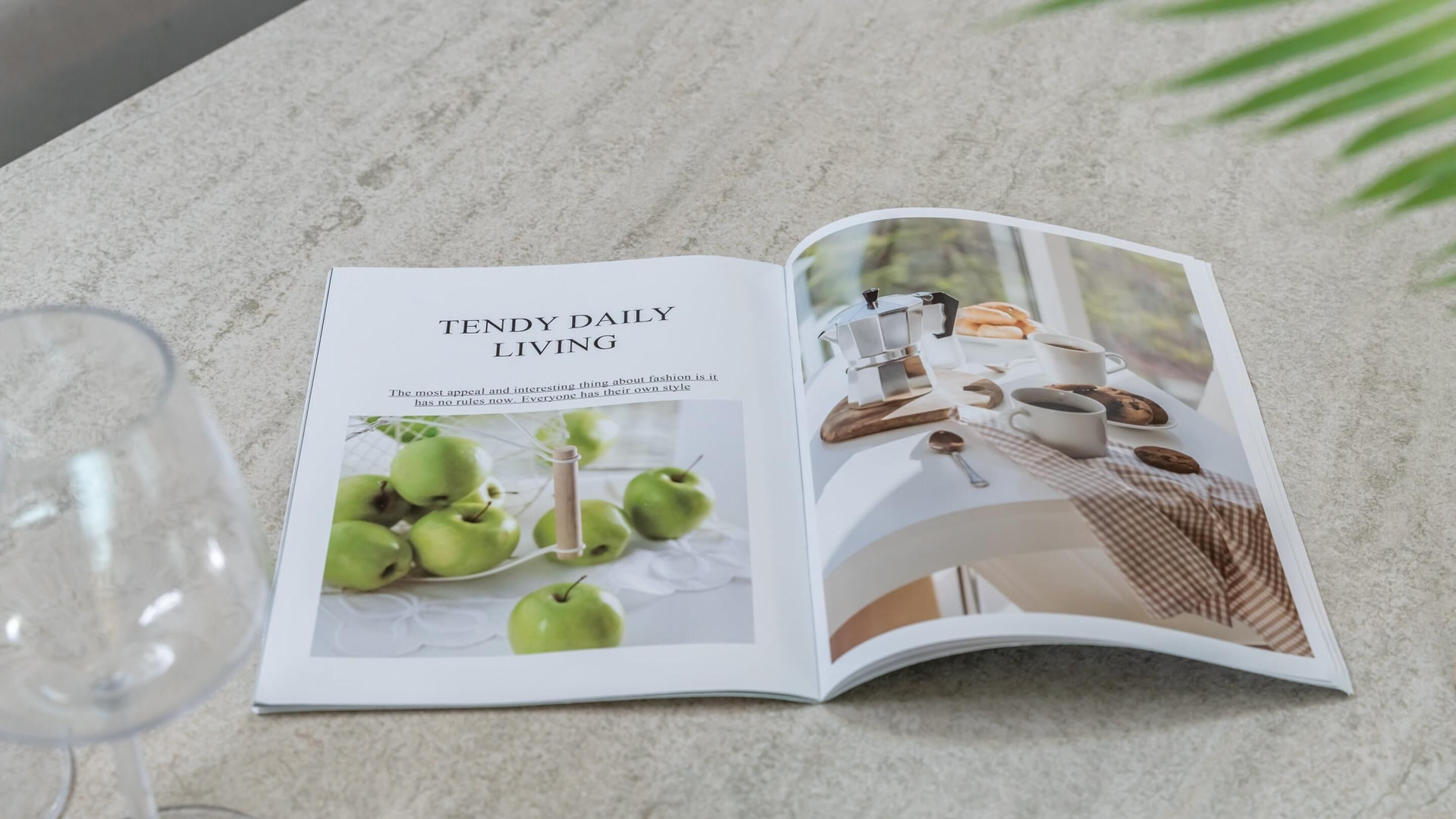 A magazine open on a marble surface, featuring a section titled "TENDY DAILY LIVING" with an image of green apples and a coffee setup.