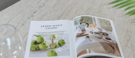 A magazine open on a marble surface, featuring a section titled "TENDY DAILY LIVING" with an image of green apples and a coffee setup.
