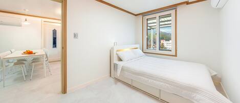 A bedroom with a bed, a window with a view, a desk with chairs, and a door leading to another room.