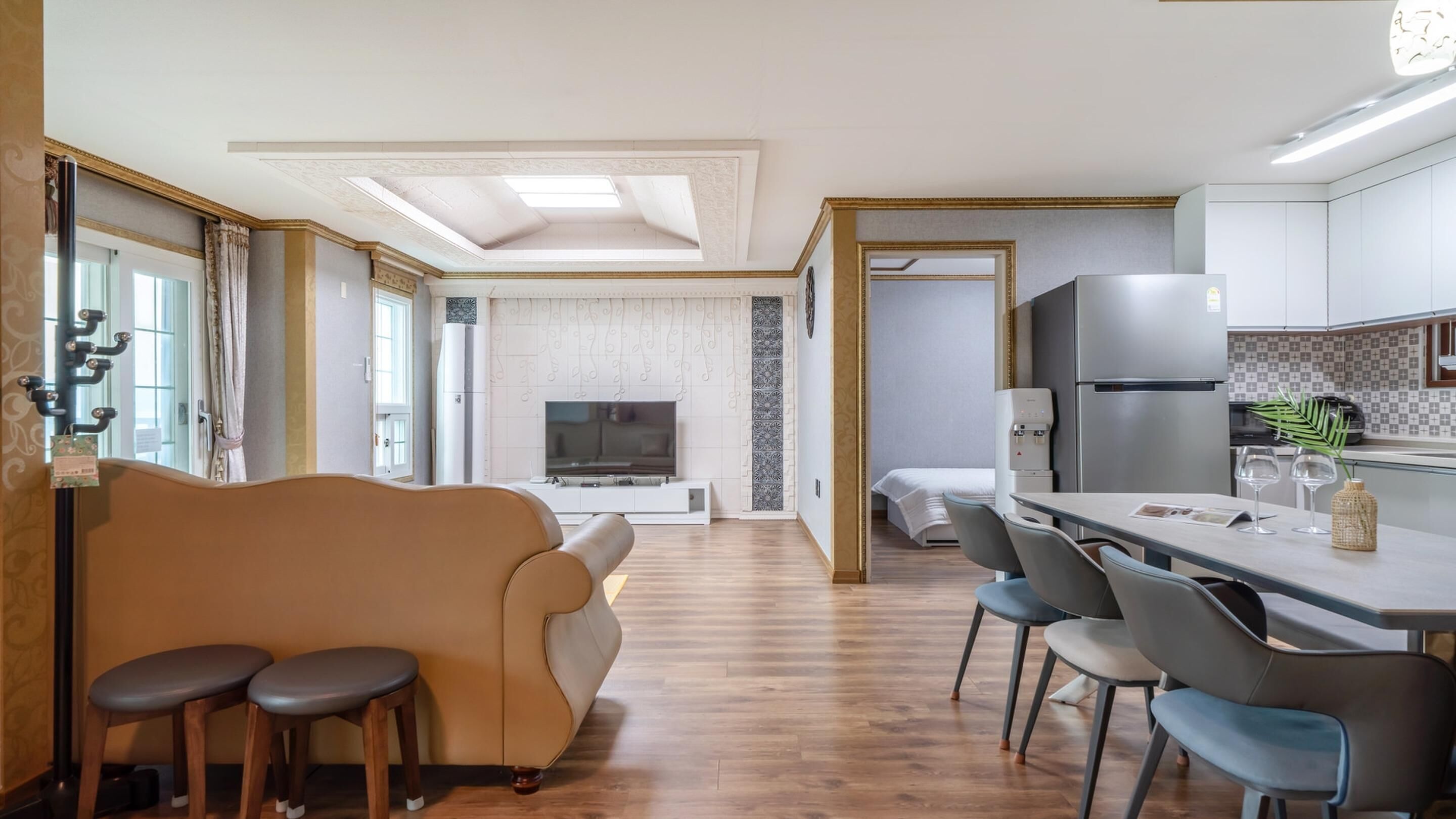 Una cocina moderna con una isla central, un comedor con sillas y una sala de estar con sofá y televisor.