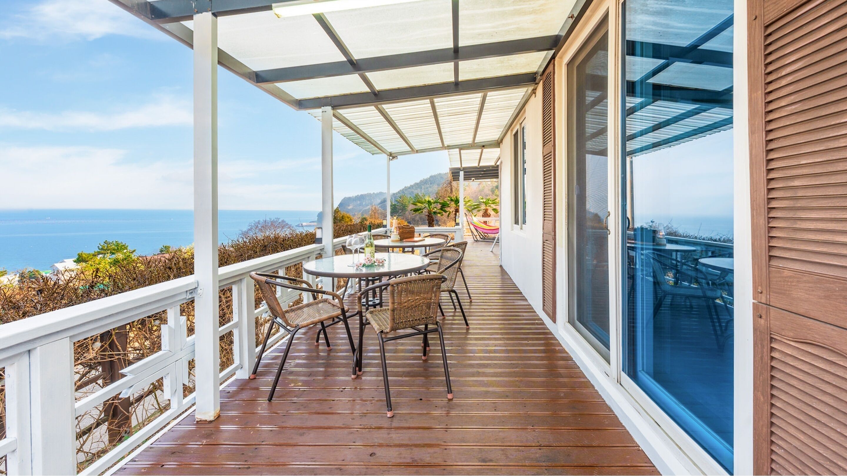 A covered outdoor area with a wooden deck, wicker furniture, and a table set for dining.
