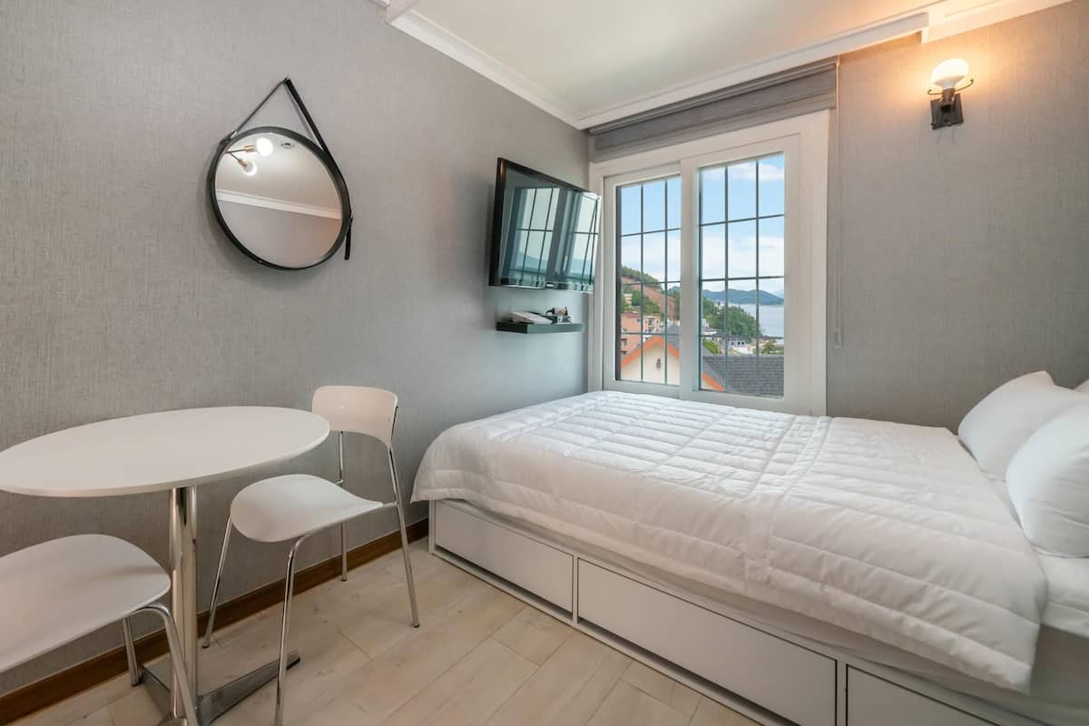 A bedroom with a bed, a round table with chairs, a mirror, and a TV on the wall.