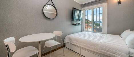 Un dormitorio con cama, una mesa redonda con sillas, un espejo y un televisor en la pared.
