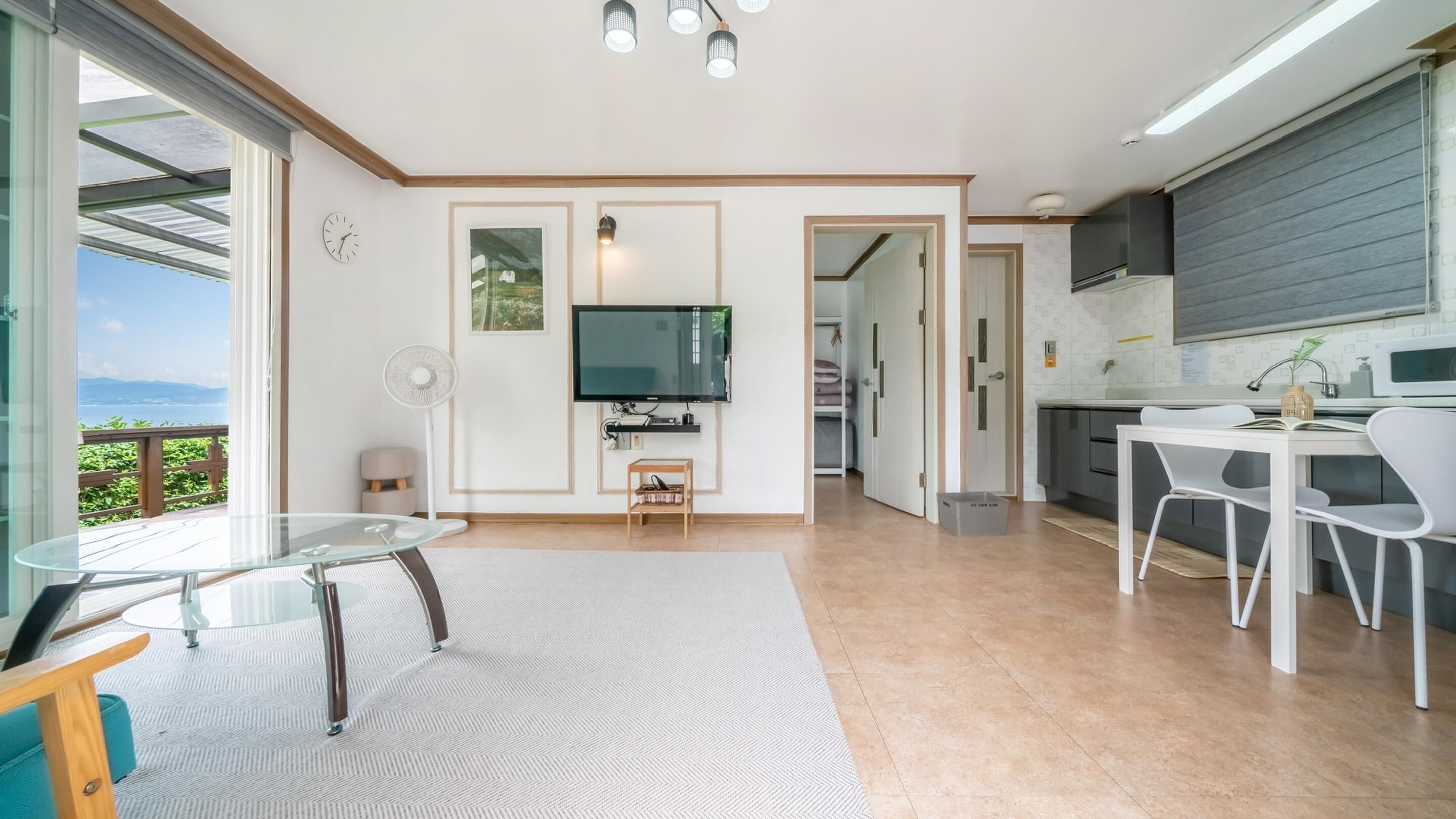 A modern kitchen with a flat-screen TV, white dining area, and a view of the outdoors.