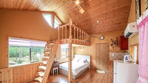 Un accogliente chalet con camera da letto soppalcata, una scala in legno, angolo cottura e una grande finestra con vista sulla natura.