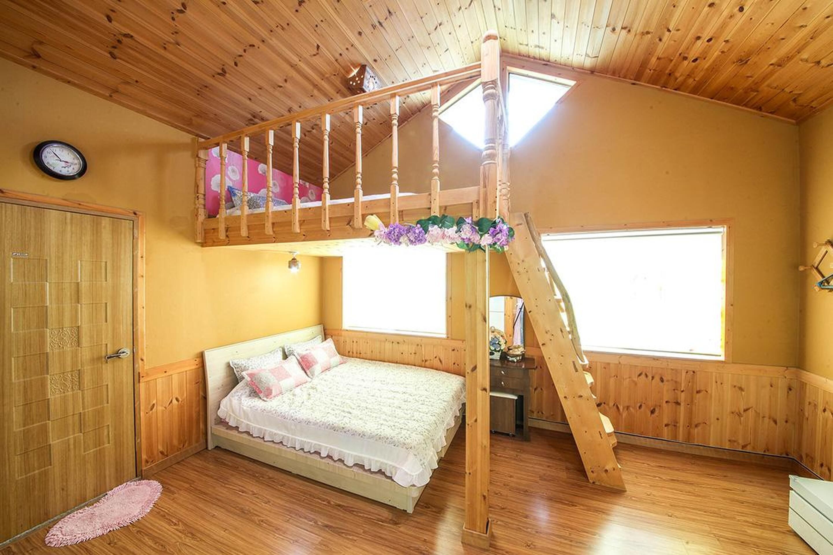 Un dormitorio con una cama litera de madera, techo de madera, un ventanal grande y una puerta de madera.