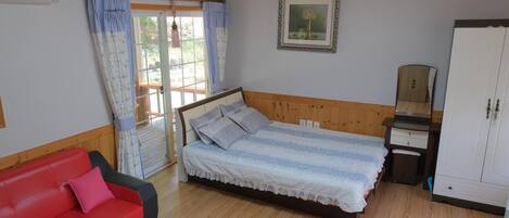 A bedroom with a bed, a red sofa, a wooden wardrobe, and a window with curtains.