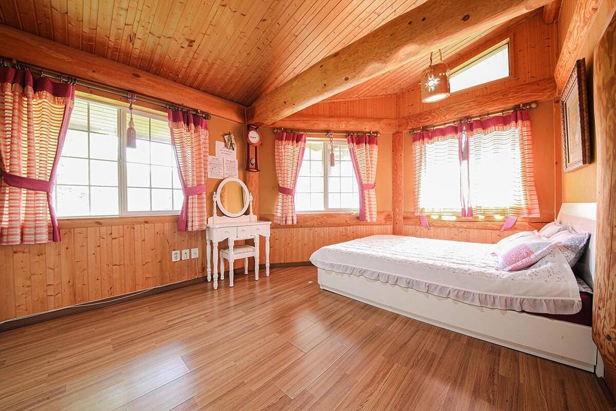 A wooden-paneled room with a bed, a vanity with a mirror, and curtains on the windows.