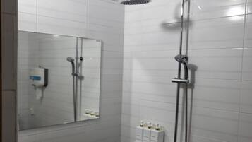 Un baño moderno con azulejos blancos, un espejo grande, una ducha con cabezal de ducha manual y un estante con artículos de tocador.