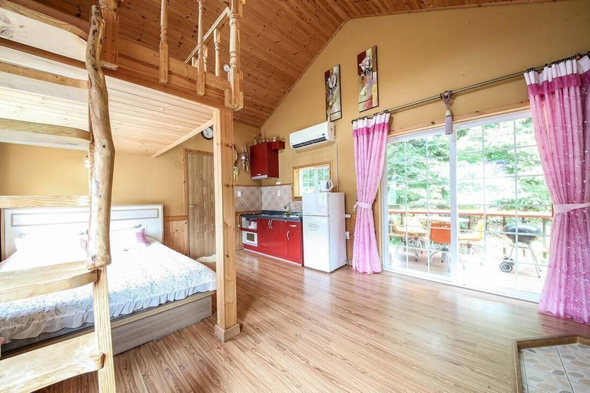 A room with a bunk bed, a kitchenette, and a large window with curtains.