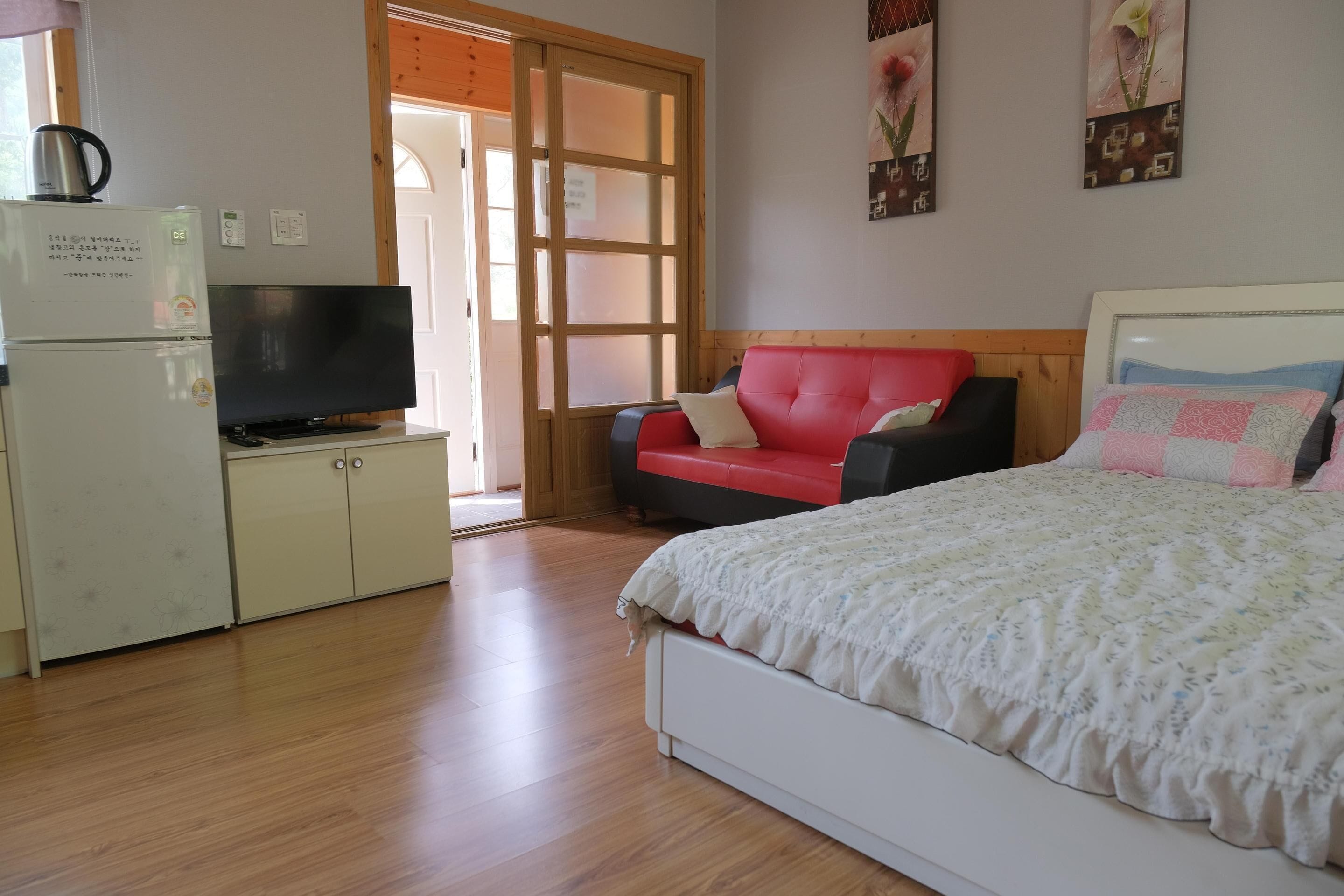 A bedroom with a bed, a TV, a refrigerator, and a red chair.