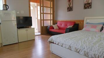A bedroom with a bed, a TV, a refrigerator, and a red chair.
