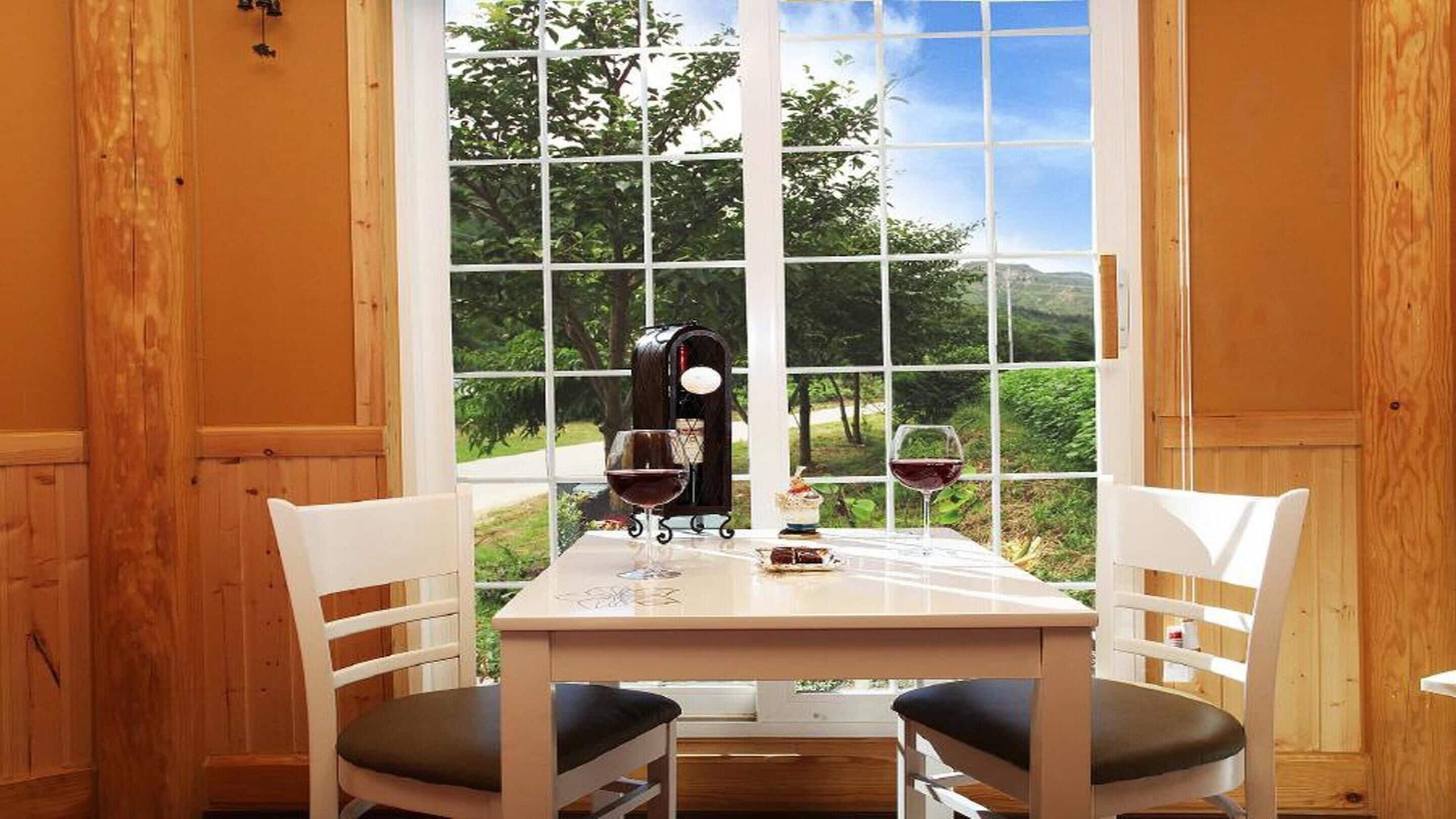 Une pièce aux murs lambrés, avec une table dressée pour deux personnes, comprenant un réfrigérateur à vin, deux verres à vin et une petite assiette de nourriture.
