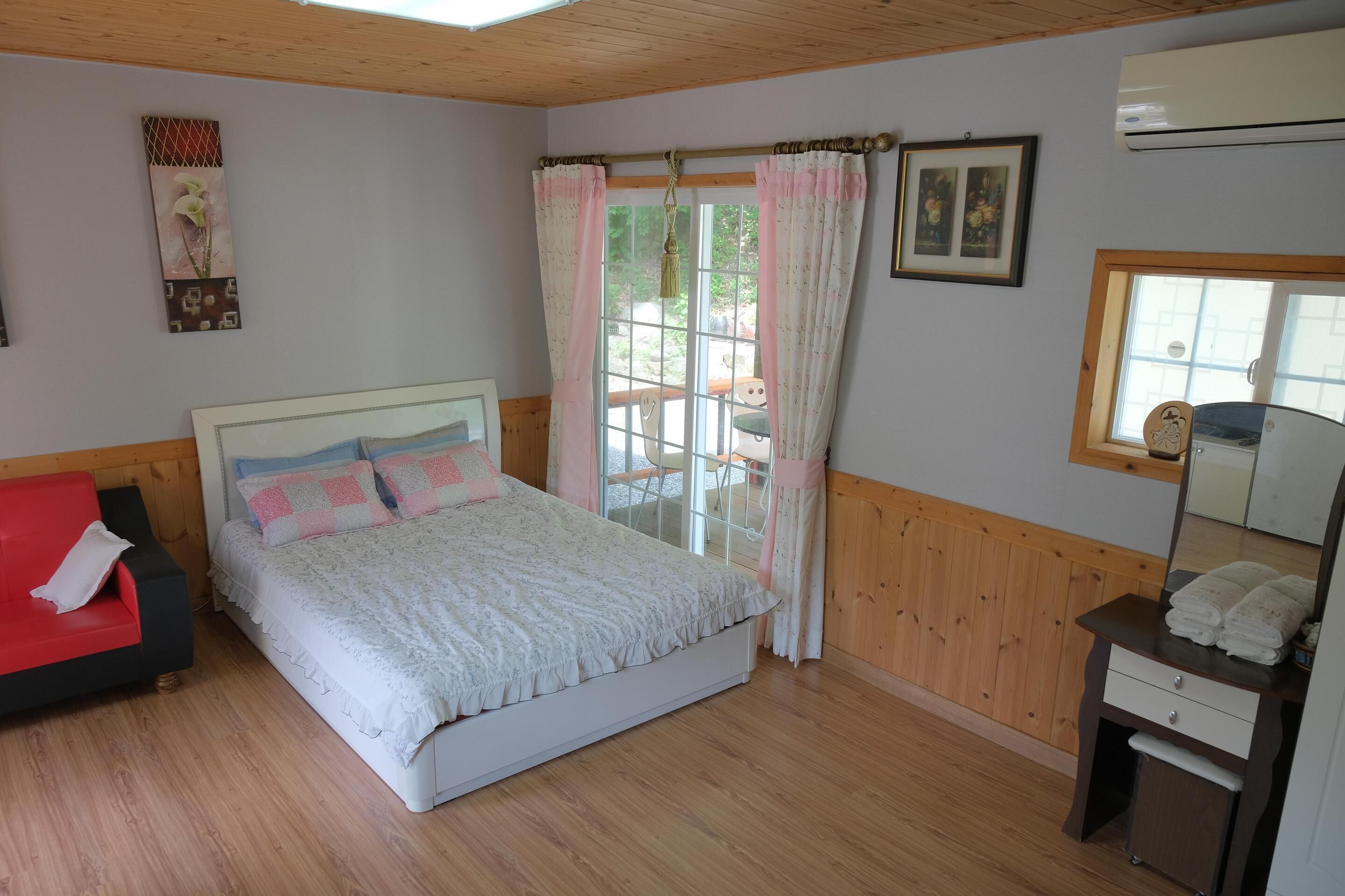 Un dormitorio con una cama, un sofá rojo, un aparador de madera y una ventana con cortinas.