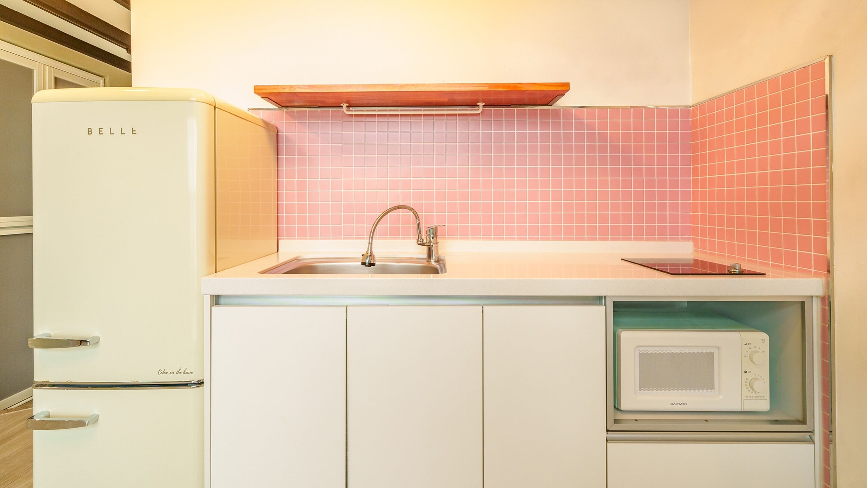 Una cucina compatta con frigorifero bianco, lavello e rubinetto, forno a microonde e zoccolo backsplash in piastrelle rosa.