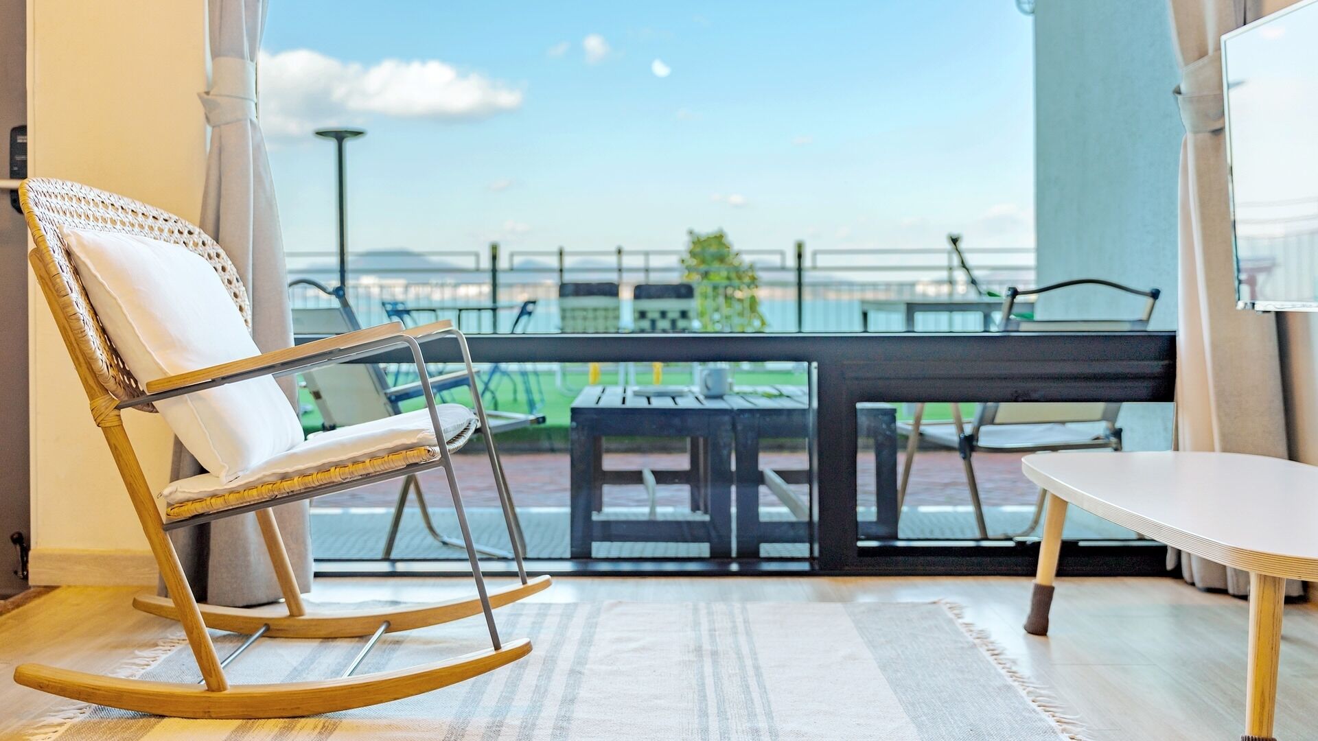 Un balcon avec un fauteuil à bascule en osier, une table et une vue sur un terrain de sport.