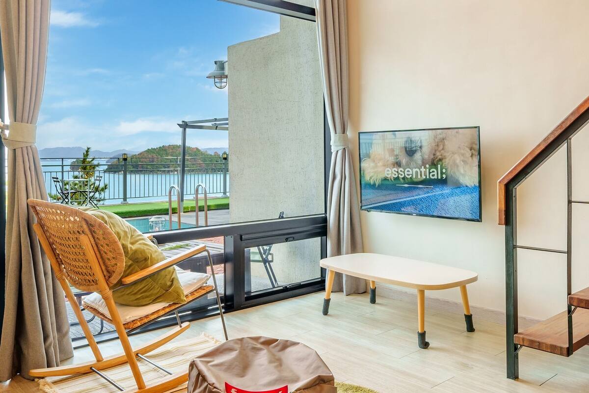 A balcony with a view of a body of water, a wooden rocking chair, a small table, and a staircase.