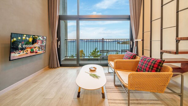 Una sala de estar moderna con un ventanal grande, un televisor de pantalla plana, muebles de mimbre y vista al mar.
