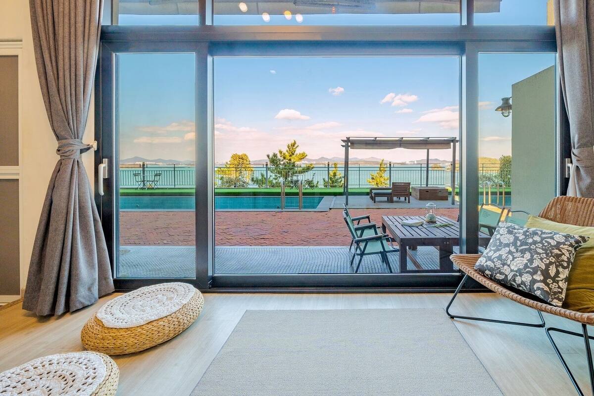 A room with a large sliding glass door leading to an outdoor patio with a pool, seating, and a pergola.