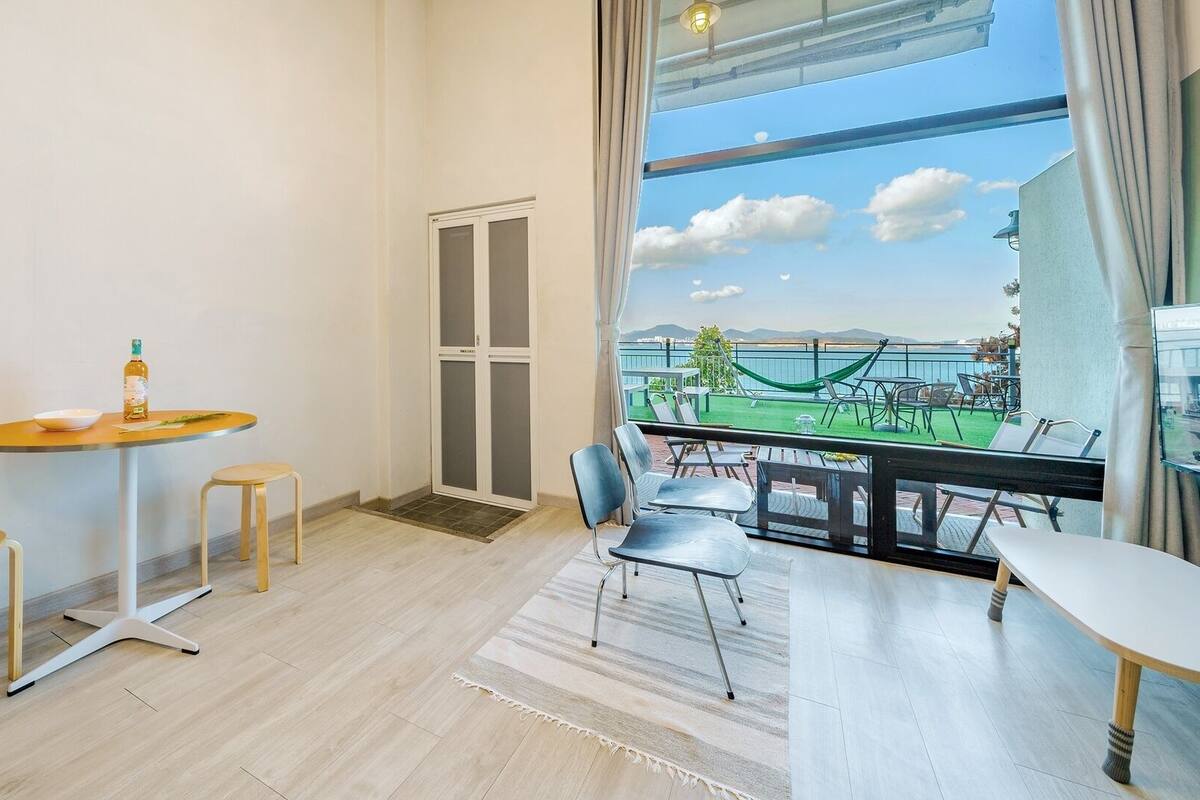 A modern room with a balcony, a dining area, and a view of a green landscape.