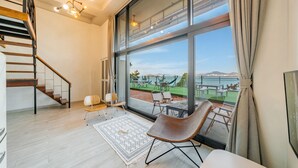 Amplia habitación con un gran ventanal, una escalera de madera y vistas a un patio exterior con mobiliario.
