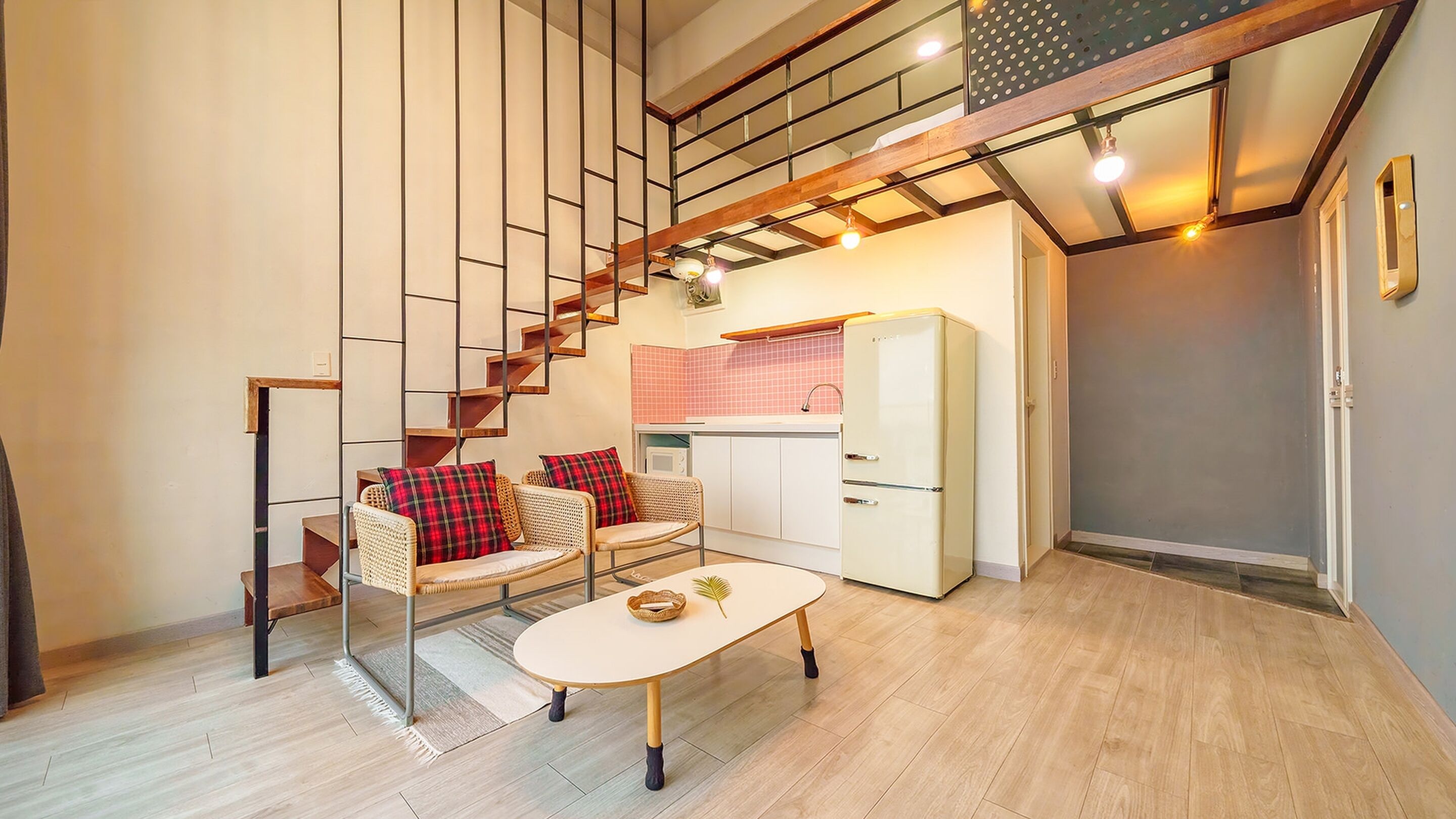 A compact living space with a staircase leading to an upper level, a kitchenette, and a seating area with two chairs and a table.