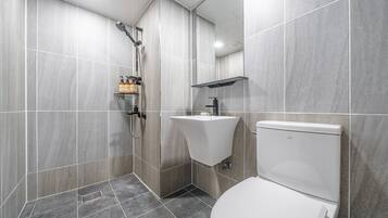 A modern bathroom with grey tiles, a shower, a sink, and a toilet.