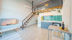 Un appartement moderne doté d’un escalier, d’une cuisine aux carreaux verts, d’un coin repas et d’un téléviseur affichant le mot « essentiel ».